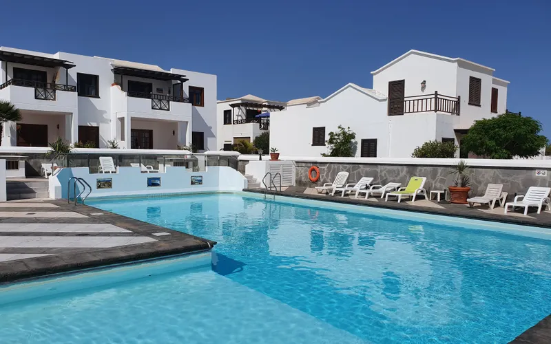Large shared swimming pool at Casa Sol y Playa with sunloungers and whitewashed complex buildings behind